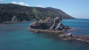 La macchina fotografica sta volando intorno alla piccola isola rocciosa in mare vicino alla riva, l'acqua del turchese del Medite video d archivio La macchina fotografica sta volando intorno alla piccola isola rocciosa in mare vicino alla riva, l'acqua del turchese del Medite video d archivio