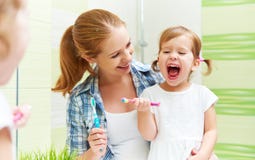 La madre della famiglia e la ragazza felici del bambino pulisce i denti con lo spazzolino da denti immagine stock libera da diritti La madre della famiglia e la ragazza felici del bambino pulisce i denti con lo spazzolino da denti immagine stock libera da diritti