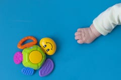La main nouveau-n?e d'enfant en bas ?ge s'?tend vers la droite au jouet d'une tortue multicolore avec un sourire sur un fond bleu images stock La main nouveau-n?e d'enfant en bas ?ge s'?tend vers la droite au jouet d'une tortue multicolore avec un sourire sur un fond bleu images stock