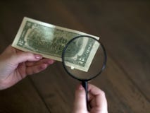 La main tient les deux dollars heureux, vus par une loupe photos stock La main tient les deux dollars heureux, vus par une loupe photos stock