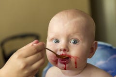 La maman alimente un enfant d'une cuillère avec du jus de framboise image stock La maman alimente un enfant d'une cuillère avec du jus de framboise image stock
