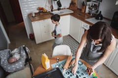 La mamma ed suo figlio cucinano i biscotti nella cucina domestica accogliente Accanto loro che guardano un neonato fotografia stock libera da diritti La mamma ed suo figlio cucinano i biscotti nella cucina domestica accogliente Accanto loro che guardano un neonato fotografia stock libera da diritti