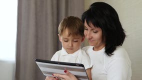 La mamá y su niño pasan tiempo en la tableta en casa, jugando y mirando las historietas, jugando a los videojuegos, usando metrajes La mamá y su niño pasan tiempo en la tableta en casa, jugando y mirando las historietas, jugando a los videojuegos, usando metrajes