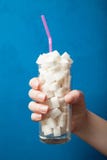 La manière au diabète - la main tient un verre avec beaucoup de sucre blanc de raffinage, en gros plan photographie stock La manière au diabète - la main tient un verre avec beaucoup de sucre blanc de raffinage, en gros plan photographie stock