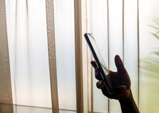 La mano de la persona que sostiene un teléfono móvil dentro, al lado de una ventana imagenes de archivo La mano de la persona que sostiene un teléfono móvil dentro, al lado de una ventana imagenes de archivo
