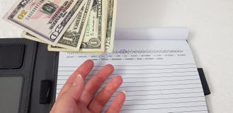 La mano femenina alcanza para los billetes de banco del dólar sobre el cuaderno abierto fotografía de archivo libre de regalías La mano femenina alcanza para los billetes de banco del dólar sobre el cuaderno abierto fotografía de archivo libre de regalías