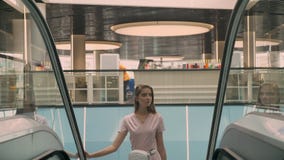 La muchacha atractiva joven aparece en la escalera móvil en la alameda, concepto que hace compras, concepto de la moda almacen de metraje de vídeo La muchacha atractiva joven aparece en la escalera móvil en la alameda, concepto que hace compras, concepto de la moda almacen de metraje de vídeo