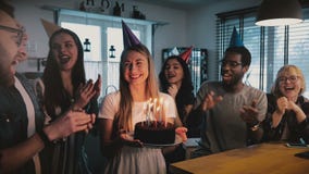 La muchacha caucásica emocionada feliz que sostiene la torta de cumpleaños, los amigos multiétnicos canta una canción alegre en l almacen de video La muchacha caucásica emocionada feliz que sostiene la torta de cumpleaños, los amigos multiétnicos canta una canción alegre en l almacen de video