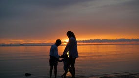 La muchacha con los niños va para los paseos y el juego en la playa en el tiempo de la puesta del sol almacen de video La muchacha con los niños va para los paseos y el juego en la playa en el tiempo de la puesta del sol almacen de video