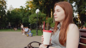 La muchacha del pelirrojo bebe el café en el parque almacen de video La muchacha del pelirrojo bebe el café en el parque almacen de video