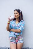 La muchacha en la ciudad en camisa que bebe un batido de leche, jugo fresco, gozando, morenita, maquillaje bronceado, sensual, re Fotografía de archivo libre de regalías