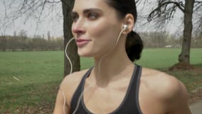 La muchacha feliz joven del deporte está corriendo con los auriculares en parque en el verano, forma de vida sana, concepto del d metrajes La muchacha feliz joven del deporte está corriendo con los auriculares en parque en el verano, forma de vida sana, concepto del d metrajes