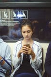 La muchacha linda monta en el subterráneo y mira la pantalla del smartphone fotografía de archivo La muchacha linda monta en el subterráneo y mira la pantalla del smartphone fotografía de archivo