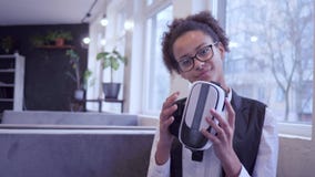 La muchacha pelada oscura sonriente del adolescente en los vidrios pone en máscara de la realidad virtual en cámara almacen de video La muchacha pelada oscura sonriente del adolescente en los vidrios pone en máscara de la realidad virtual en cámara almacen de video