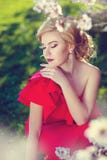 La muchacha rubia hermosa en un vestido rojo cuesta sobre la flor blanca imágenes de archivo libres de regalías La muchacha rubia hermosa en un vestido rojo cuesta sobre la flor blanca imágenes de archivo libres de regalías