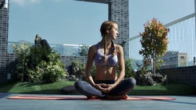 La muchacha se sienta en actitud de la yoga en terraza del resto con los céspedes La muchacha se sienta en actitud de la yoga en terraza del resto con los céspedes