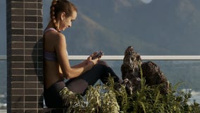 La muchacha se sienta en Internet de las resacas de la terraza en Smartphone La muchacha se sienta en Internet de las resacas de la terraza en Smartphone