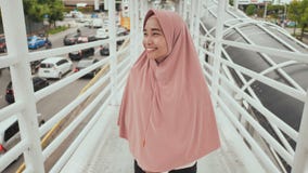 La muchacha sonriente en hijab va detrás de la cámara en la transición sobre tráfico por carretera jakarta indonesia almacen de video La muchacha sonriente en hijab va detrás de la cámara en la transición sobre tráfico por carretera jakarta indonesia almacen de video