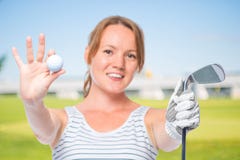 La muchacha sonriente muestra una cámara en la bola y un club de golf fotos de archivo libres de regalías La muchacha sonriente muestra una cámara en la bola y un club de golf fotos de archivo libres de regalías