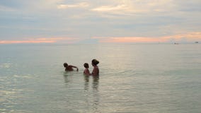 La muchacha y los niños nadan y juegan en el mar Tiempo de la puesta del sol almacen de video La muchacha y los niños nadan y juegan en el mar Tiempo de la puesta del sol almacen de video