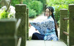 La mujer china asiática en el vestido azul y blanco tradicional de Hanfu, juego en un jardín famoso, se sienta en el puente foto de archivo La mujer china asiática en el vestido azul y blanco tradicional de Hanfu, juego en un jardín famoso, se sienta en el puente foto de archivo