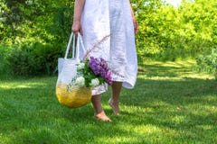 La mujer de la Edad Media en el vestido de lino simple blanco permanece descalzo en la hierba en jard?n hermoso y sostiene el bol imagenes de archivo La mujer de la Edad Media en el vestido de lino simple blanco permanece descalzo en la hierba en jard?n hermoso y sostiene el bol imagenes de archivo