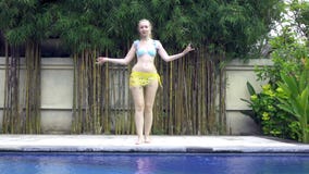 La mujer delgada joven baila una danza oriental cerca de piscina en el centro turístico tropical, cámara lenta almacen de video La mujer delgada joven baila una danza oriental cerca de piscina en el centro turístico tropical, cámara lenta almacen de video