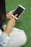 La mujer en la camisa que jugaba en el tel?fono, sent?ndose en un piso verde con las piernas cruz? imagen de archivo La mujer en la camisa que jugaba en el tel?fono, sent?ndose en un piso verde con las piernas cruz? imagen de archivo