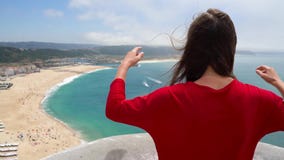 La mujer en vestido rojo disfruta de una vista de la costa del océano cerca de Nazare, Portugal almacen de metraje de vídeo La mujer en vestido rojo disfruta de una vista de la costa del océano cerca de Nazare, Portugal almacen de metraje de vídeo