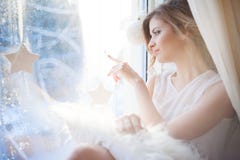 la mujer hermosa con maquillaje diario fresco y el peinado ondulado romántico, sentándose en el alféizar, dibuja sobre el vidrio imagen de archivo libre de regalías la mujer hermosa con maquillaje diario fresco y el peinado ondulado romántico, sentándose en el alféizar, dibuja sobre el vidrio imagen de archivo libre de regalías