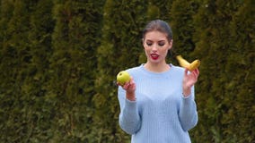 La mujer joven atractiva del retrato en chaqueta azul elige entre la manzana y el plátano verdes La mujer joven atractiva del retrato en chaqueta azul elige entre la manzana y el plátano verdes
