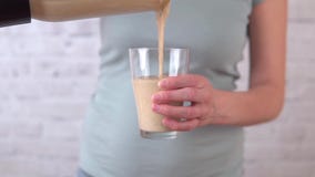 La mujer joven en una cocina está vertiendo el smoothie amarillo del plátano de la licuadora al vidrio almacen de metraje de vídeo La mujer joven en una cocina está vertiendo el smoothie amarillo del plátano de la licuadora al vidrio almacen de metraje de vídeo