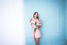 La mujer joven hermosa en la tenencia rosada del vestido en manos salta ramo de las flores de los tulipanes en fondo azul de la p imágenes de archivo libres de regalías La mujer joven hermosa en la tenencia rosada del vestido en manos salta ramo de las flores de los tulipanes en fondo azul de la p imágenes de archivo libres de regalías
