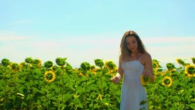 La mujer joven linda del primer con el pelo marrón largo y en los sundress blancos del verano camina en campo ilustrado con los g metrajes La mujer joven linda del primer con el pelo marrón largo y en los sundress blancos del verano camina en campo ilustrado con los g metrajes