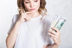 La mujer joven pensativa mira el manojo de dinero, piensa donde gastarlo, sobre el fondo blanco imagen de archivo libre de regalías La mujer joven pensativa mira el manojo de dinero, piensa donde gastarlo, sobre el fondo blanco imagen de archivo libre de regalías