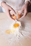 La mujer joven rompe el huevo sobre la harina blanca para hacer la pasta para las pastas italianas, para los raviolis o los talla imagen de archivo libre de regalías La mujer joven rompe el huevo sobre la harina blanca para hacer la pasta para las pastas italianas, para los raviolis o los talla imagen de archivo libre de regalías