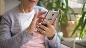 La mujer madura está sosteniendo el smartphone, música que escucha almacen de metraje de vídeo La mujer madura está sosteniendo el smartphone, música que escucha almacen de metraje de vídeo