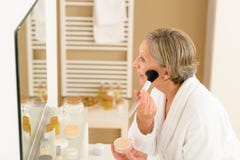 La mujer mayor aplica el polvo del maquillaje en cuarto de baño imagen de archivo La mujer mayor aplica el polvo del maquillaje en cuarto de baño imagen de archivo
