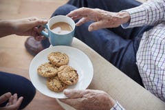 La mujer pasa el té y las galletas a un hombre mayor asentado, detalle imagen de archivo libre de regalías La mujer pasa el té y las galletas a un hombre mayor asentado, detalle imagen de archivo libre de regalías