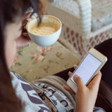 La mujer que bebe el café caliente en café y utiliza un teléfono móvil imagen de archivo libre de regalías La mujer que bebe el café caliente en café y utiliza un teléfono móvil imagen de archivo libre de regalías