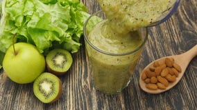 La mujer que vierte un jugo verde del detox de la licuadora a un tarro, en casa deporte que lleva viste La mujer que vierte un jugo verde del detox de la licuadora a un tarro, en casa deporte que lleva viste