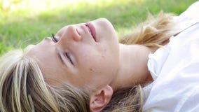 La mujer rubia joven con los ojos azules hermosos está mintiendo en la hierba en el parque almacen de metraje de vídeo La mujer rubia joven con los ojos azules hermosos está mintiendo en la hierba en el parque almacen de metraje de vídeo