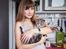 La mujer rubia joven feliz en la camiseta casual que detiene a escocés magnífico dobla el gato en la cocina nacional Retrato natu fotografía de archivo La mujer rubia joven feliz en la camiseta casual que detiene a escocés magnífico dobla el gato en la cocina nacional Retrato natu fotografía de archivo