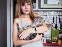 La mujer rubia joven feliz en la camiseta casual que detiene a escocés magnífico dobla el gato en la cocina nacional Retrato natu fotos de archivo libres de regalías La mujer rubia joven feliz en la camiseta casual que detiene a escocés magnífico dobla el gato en la cocina nacional Retrato natu fotos de archivo libres de regalías