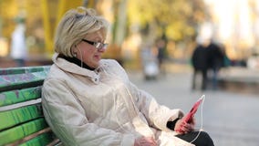 La mujer se sienta en el banco en el parque de la ciudad y comunica vía smartphone rojo metrajes La mujer se sienta en el banco en el parque de la ciudad y comunica vía smartphone rojo metrajes