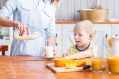 La mère et le fils sourient tout en prenant un petit déjeuner dans la cuisine La maman verse le lait dans le verre photo stock La mère et le fils sourient tout en prenant un petit déjeuner dans la cuisine La maman verse le lait dans le verre photo stock