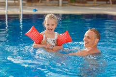 La nadada del papá y de la hija en la piscina, y ella ríe hacia fuera ruidosamente y s foto de archivo libre de regalías La nadada del papá y de la hija en la piscina, y ella ríe hacia fuera ruidosamente y s foto de archivo libre de regalías