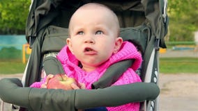 La neonata si siede in un passeggiatore di bambino e mangia una mela video d archivio La neonata si siede in un passeggiatore di bambino e mangia una mela video d archivio