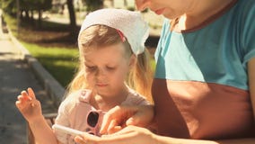 La niña está jugando en un smartphone que miente en las manos de su mamá al aire libre La niña está jugando en un smartphone que miente en las manos de su mamá al aire libre