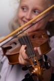 La niña linda en blusa brillante juega el primer del violín en un fondo gris foto de archivo La niña linda en blusa brillante juega el primer del violín en un fondo gris foto de archivo